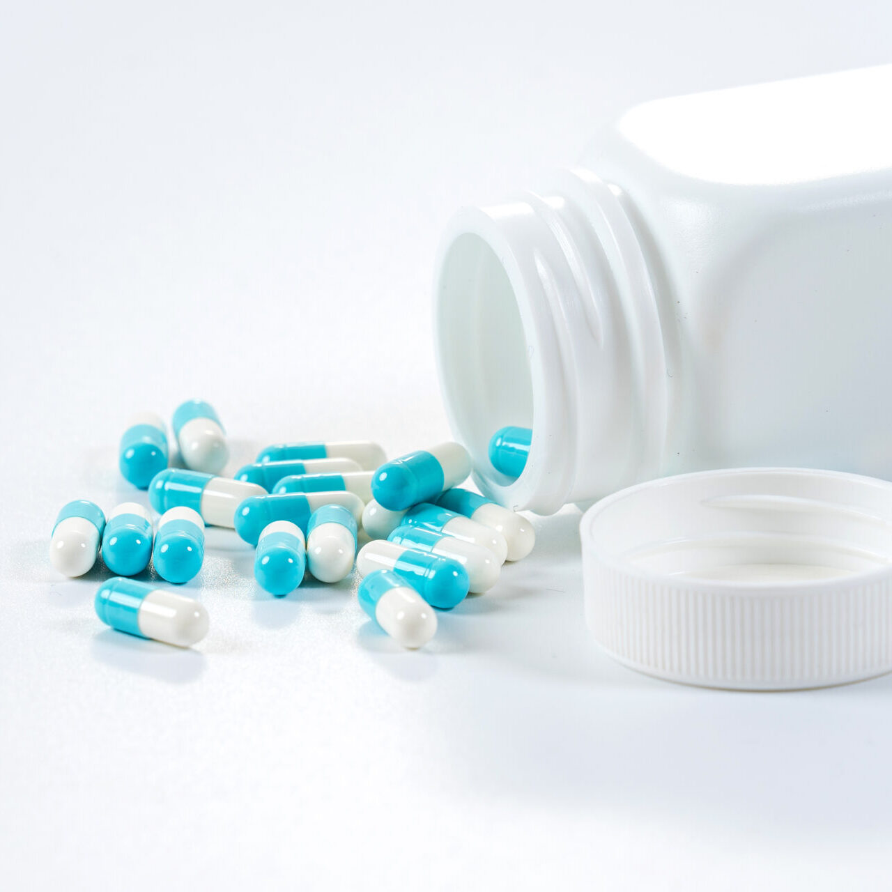 blue-white-capsules-pills-pouring-from-bottle-white-background-scaled.jpg